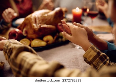 Close up of kid holding hands with his family while praying before Thanksgiving meal at home. - Powered by Shutterstock