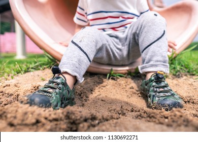 Close Up Of Kid Rubber Shoes, Kid Hiking Shoes, Adventure Shoes On Child Feet Steps On Wet Sands At Kid Play Ground