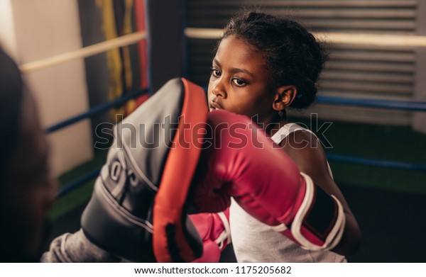 Close up of
a kid training inside a boxing ring. Kid boxer wearing boxing
gloves practicing punches on a punching
pad.