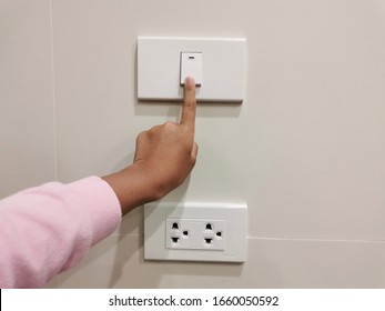 Close Up Finger’s Kid Is Turning On Or Turning Off The Light-switch. Electrical Socket And Light-switch On Wall. Child At Risk Of Electric Shock. Safety Concept.