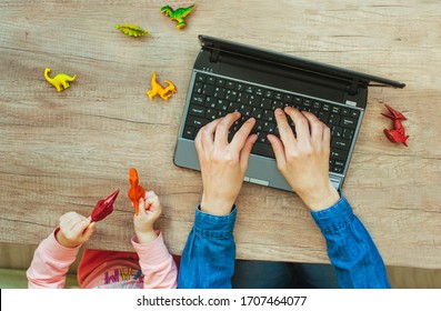 Close up of kids hands playing with dinosaur toys while sitting near mother typing on the laptop on wooden background. Work from home during quarantine concept. Top view, flat lay. - Powered by Shutterstock