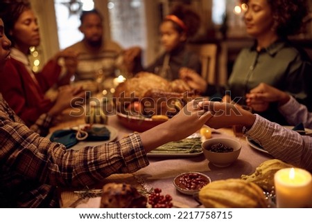 Close of kids saying grace while having Thanksgiving dinner with their family at dining table. 