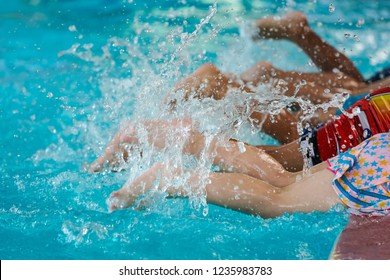 Close Up Kids Training Legs At Swimming Pool Class Learning To Swim With Swimming Teacher.