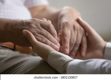 Close Up Kind Caregiver Medical Worker Holding Hands Of Old 70s Retired Patient, Supporting At Curing Cancer At Meeting. Compassionate Young Doctor Giving Psychological Help To Elder Mature Man.