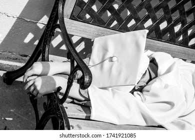 Close Up Of Kindergarten Graduate Facedown Unrecognizable Wearing White Cap And Gown On A Bench Outside 