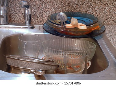 Close Up Of The Kitchen Sink With Very Messy Piles Of Dirty Dishes. The Sink Is Stainless Steel. The Dishes Are Bowls, Plates, Pans And Flatwear. Concept Of Disorganization And Clutter And Filth 