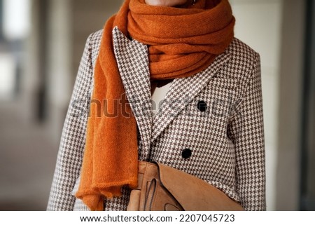 Close up knitted wool ochre scarf and double breasted houndstooth jacket with buttons. Stylish fashion trend details