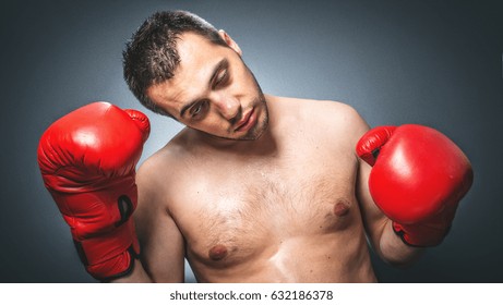 Close Up Of Knockout Boxer Over Dark Gray Background. Comic Weak Fighter With Red Sport Boxing Gloves. Waist Up Humorous Kickboxer