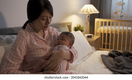 Close Up Korean First Time Mom Seated In Bedroom Is Holding And Touching Gently On Her Lovely Baby To Put Her To Sleep.