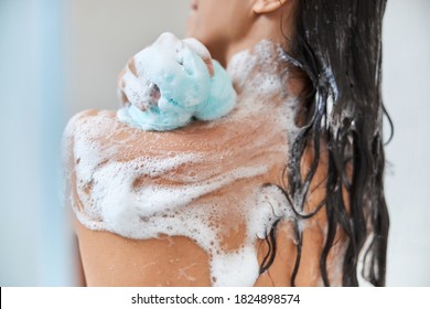 Close up of lady with foam on her skin using bath loofah while taking shower at home