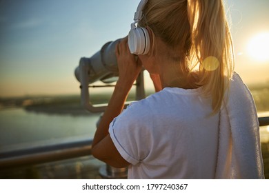 Close up of lady listening to music and looking at cityscape through stationery binoculars on observation deck