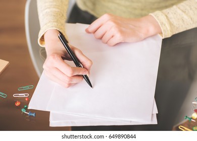 Close Up Of Lady's Hands Writing On Paper Sheets Placed On Glass Desk With Colorful Supplies And Other Items. Paperwork Concept