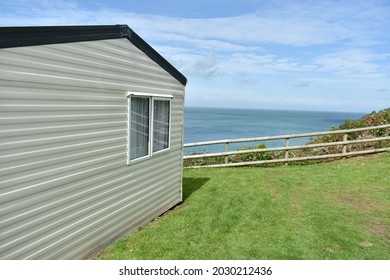 Close Up Landscape Image Of Mobile Home, Static Caravan, On Green Grass Cliff Edge With Ocean In Background On A Sunny Summers Day With Deep Blue Sky And White Clouds