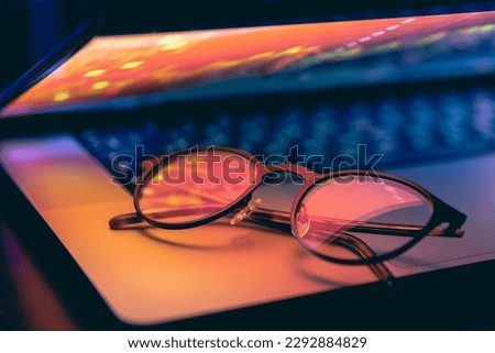 Close up of laptop keyboard colorful neon illumination and eyeglasses.