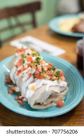 Close Up Of A Large Mexican Breakfast Burrito Smothered In Fresh Tomato Pico De Gallo Salsa And Covered With Sour Cream With Blurry Restaurant Table Background