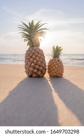 Close up  large pineapple and a small pineapple stand on the sand against the background of the sea and sunset. Photo is ideal for advertising, poster and wallpaper