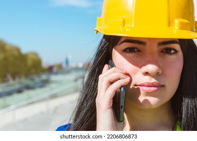 Close Up Of Latin Caucasian Venezuelan Female Construction Worker, With Yellow Helmet Is Receiving Instructions From Her Boss By Phone Call, Copy Space On The Left.