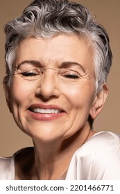 Close up of a Latina woman in her 60's smiling with her eyes closed on a neutral background. Stock Photo
