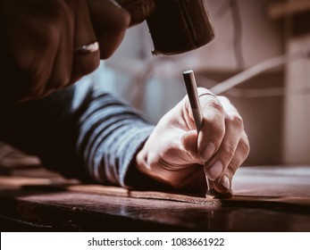 Close up of leather craftsman working with natural leather using hammer. Handbag master at work in local workshop. Handmade concept. Male shoemaker creating product with textile