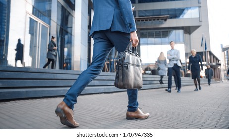 Close Up Leg Shot of a Businessman in a Suit Commuting to the Office on Foot. He's Carrying a Leather Case. Other Managers and Business People Walk Nearby. Cloudy Day on a Downtown Street. - Powered by Shutterstock