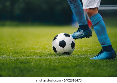 Close Up Of Legs And Feet Of Football Player In Blue Socks And Shoes Running And Dribbling With The Ball. Soccer Player Running After The Ball. Sports Venue In The Background