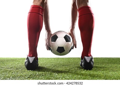 close up legs of football player in red socks and black shoes holding the ball in his hands placing it at the free kick or penalty spot playing on grass pitch isolated on white background