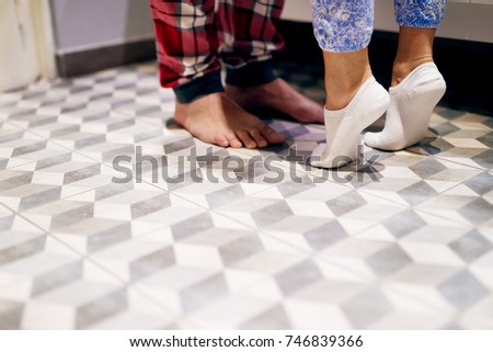 Close up of legs, a girl in socks raised feets to kiss her boyfriend while standings in pajamas.