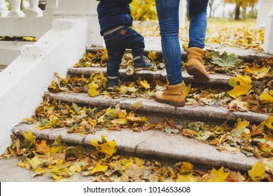 Close Up Legs Of Woman Walk In Fall Park With Little Child Boy, Climb Up Stairs With Dry Yellow Autumn Leaves. Mother, Small Kid Son Feet On Steps. Family Day 15 Of May Love Parents, Children Concept