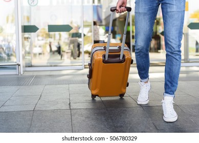 Close up of legs of young man going into the airport with suitcase