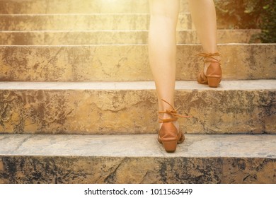 Close up legs of young woman walking stepping up stair in attractions. Feet and leg of young woman wearing brown high going up the stairs outdoors. Alone travel concept