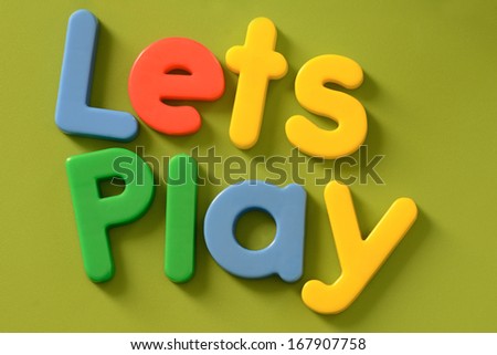 Close up of Lets Play words in colorful plastic letters on green background