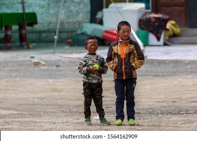 CLOSE TO LHASA, TIBET / CHINA - Aug 1, 2017: Two tibetan boys (between 5 and 8 years old) standing on the side of a street / road. One holds a tennis ball, the other is having his hands in his pocket.