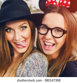 Close Up Lifestyle Portrait Of Girls Best Friends Makes Funny Grimaces On Camera , Show Tongue And Laughing Together.Two Women Posing Outdoor, Warm Sunny Evening Colors.