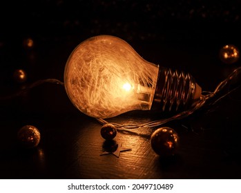 Close up of a light bulb containing tiny white featers laying on a dark surface decorated with golden glitter balls