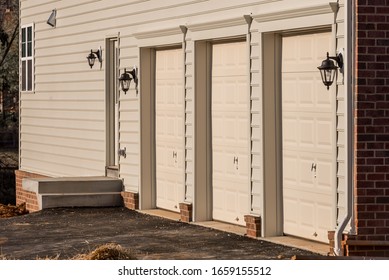 Close Up Of Light Maple Or Desert Tan Triple Single Car Insulated Steel Raised Panel Garage Door And Vinyl Horizontal Lap Siding On A Brand New Built American Home In The East Coast