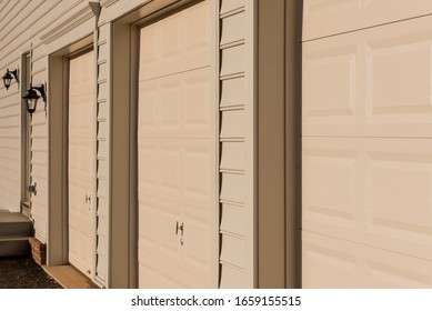 Close Up Of Light Maple Or Desert Tan Triple Single Car Insulated Steel Raised Panel Garage Door And Vinyl Horizontal Lap Siding On A Brand New Built American Home In The East Coast