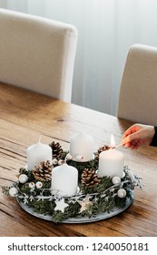 Close Up Of Lighting The First Candle On Advent Wreath On The First Sunday In December. Celebrating Christmas Holidays, Swiss Tradition. Crop Hand Holding The Safety Matches To Light The Candle. 