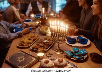 Close up of lit candles in menorah with Jewish multigeneration family celebrating Hanukkah at dining table.