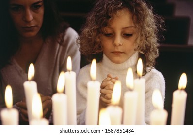 Close up of lit candles with woman and child praying Foto Stock