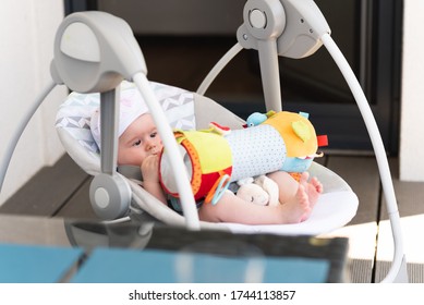 Close up of little 6 months old sweet baby girl in electric swing or cradle outdoors on sunny summer day. Infant background