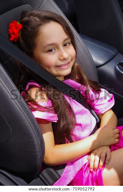 Close up
of little beatiful girl sitting in the car wearing a pink dress and
a red flower in her head using a safety
belt