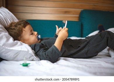 Close Up Of Little Boy Watching Cartoons On The Digital Tablet At Morning With Copy Space. Close Up Of Adorable Kid Laying Down On The Bed By Holding A Tablet. Kid In Bed Looking At The Tablet PC