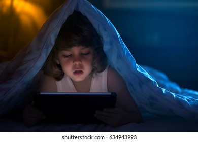 Close up of little boy watching cartoons on the digital tablet at night with copy space