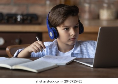 Close up little boy in wireless headphones studying online at home, looking at laptop screen, writing taking notes, 8s child kid watching webinar, listening to lecture, homeschooling concept - Powered by Shutterstock