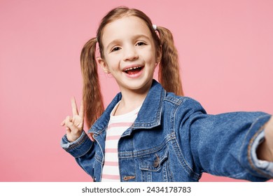 Close up little child kid girl 7-8 year old wears denim shirt do selfie shot on mobile cell phone show v-sign isolated on plain pastel light pink background. Mother's Day love family lifestyle concept