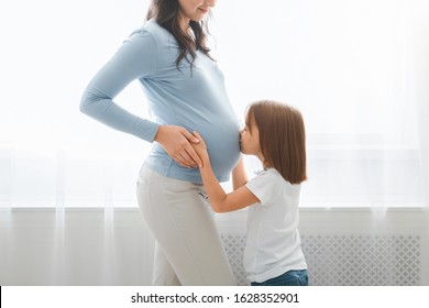 Close Up Of Little Daughter Kissing Her Pregnant Mom Tummy, White Background