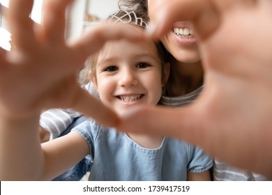 Close Up Little Girl Wearing Princess Diadem And Mother Showing Heart Sign With Hands, Looking Through Fingers At Camera, Taking Selfie, Happy Mum And Smiling Daughter Having Fun Together