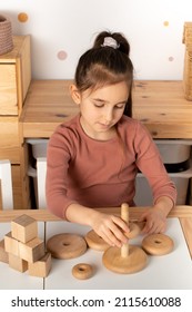 Close up of little toddler girl wearing pajamas playing with wooden toy pyramid sitting at the table in the kids room. Natural eco toys concept. girl playing with a pyramid