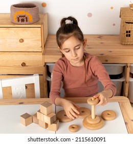 Close up of little toddler girl wearing pajamas playing with wooden toy pyramid sitting at the table in the kids room. Natural eco toys concept. girl playing with a pyramid