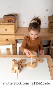 Close up of little toddler girl wearing pajamas playing with wooden toy pyramid sitting at the table in the kids room. girl playing with a pyramid